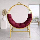 A modern hanging bubble chair with a gold metal frame and deep burgundy cushions, set in a minimalist interior room.